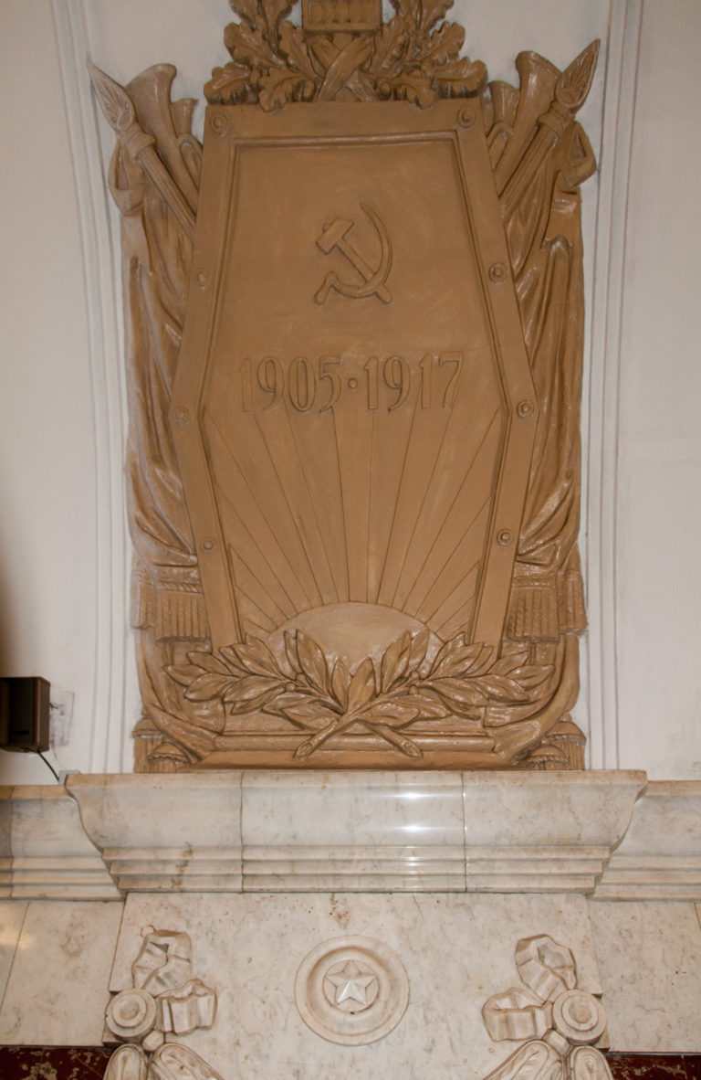 1905–1917 hammer-and-sickle relief mounted above pale marble garland decoration in a metro station.