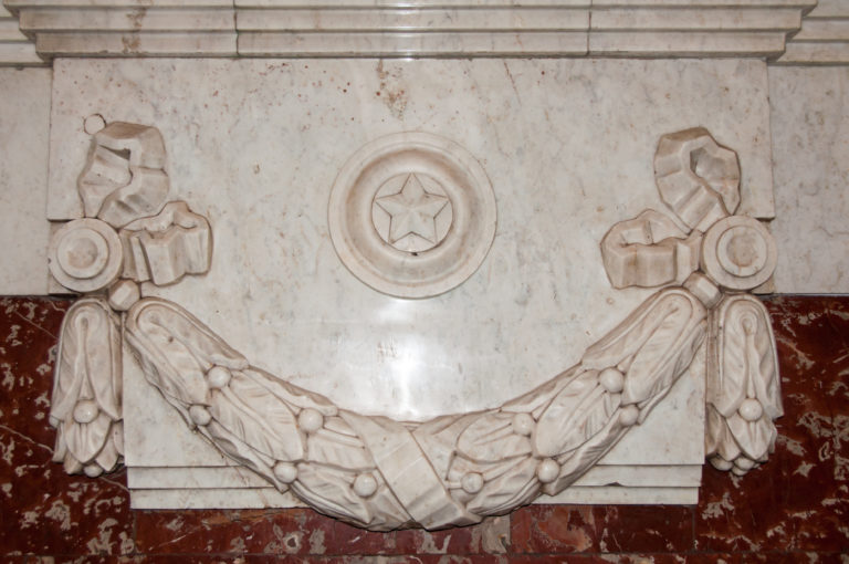 Pale carved garland and five-pointed star medallion set against marble with a dark red horizontal band.