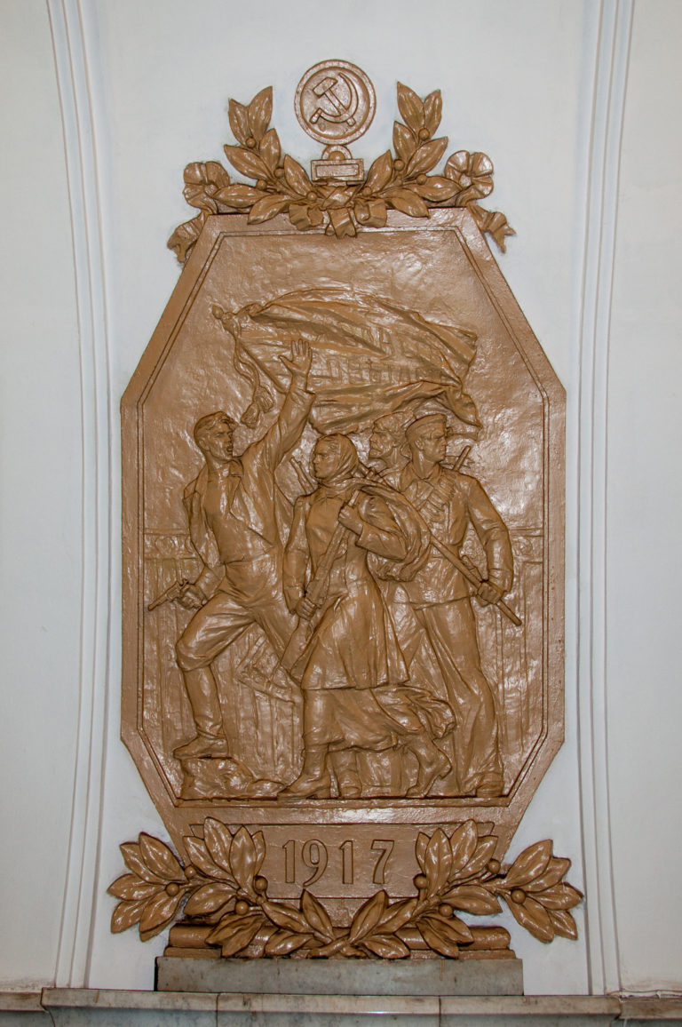 Bronze-toned 1917 relief showing armed revolutionary figures beneath a Soviet emblem and decorative foliage.