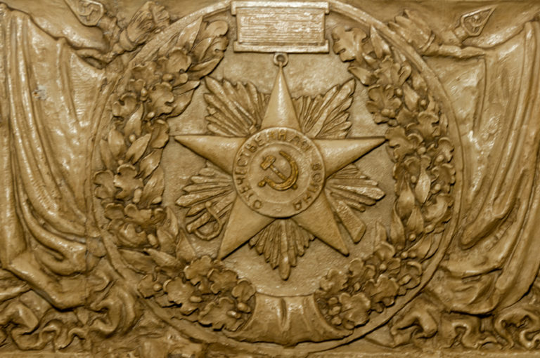 Sculpted Soviet military medal with hammer and sickle, starburst, wreath, and draped banners.