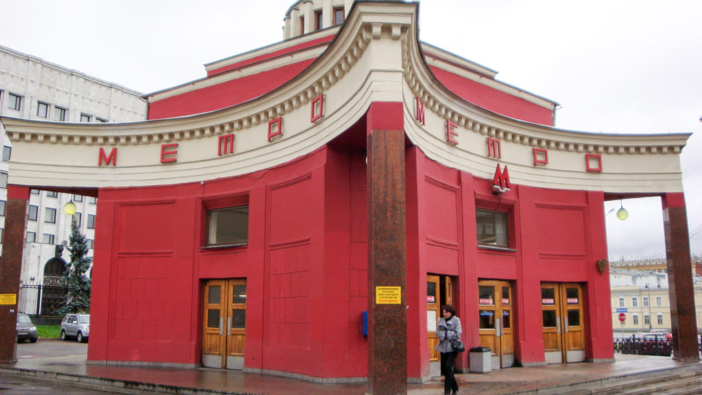 Red-and-white Moscow Metro entrance pavilion with curved façade, METRO lettering, stone piers, and wooden doors.