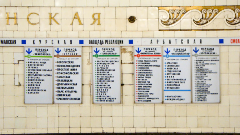 Russian-language Moscow Metro directional boards with colored arrows mounted on a pale tiled wall.
