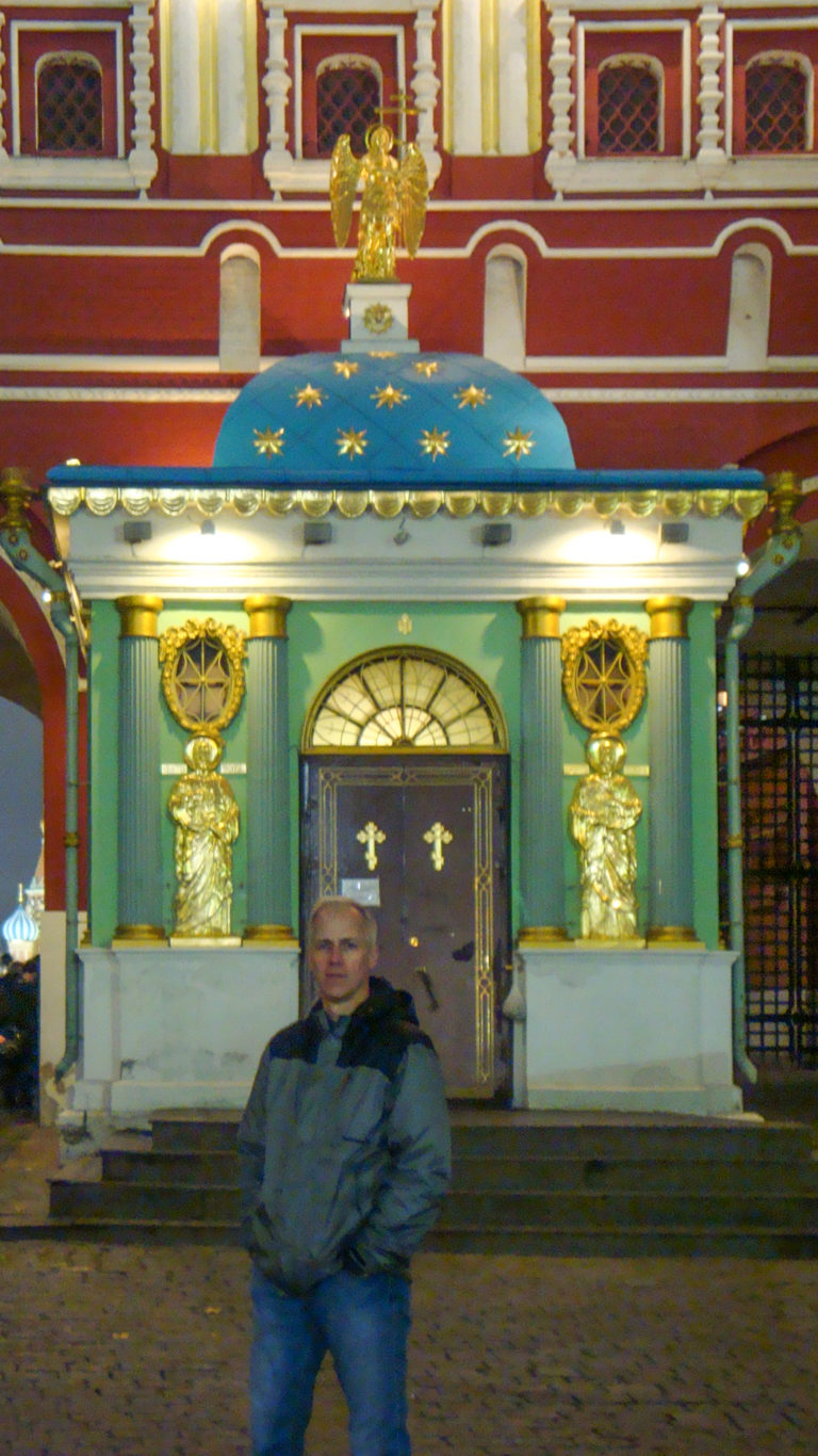 Iveron Chapel with blue star-patterned roof, green columns and gilded ornament, with a visitor standing in front.