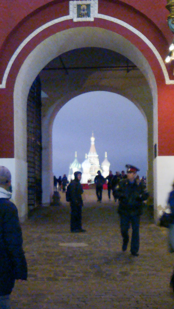 Pedestrians walk through a large red-and-white arched passage of the Resurrection Gate at twilight.