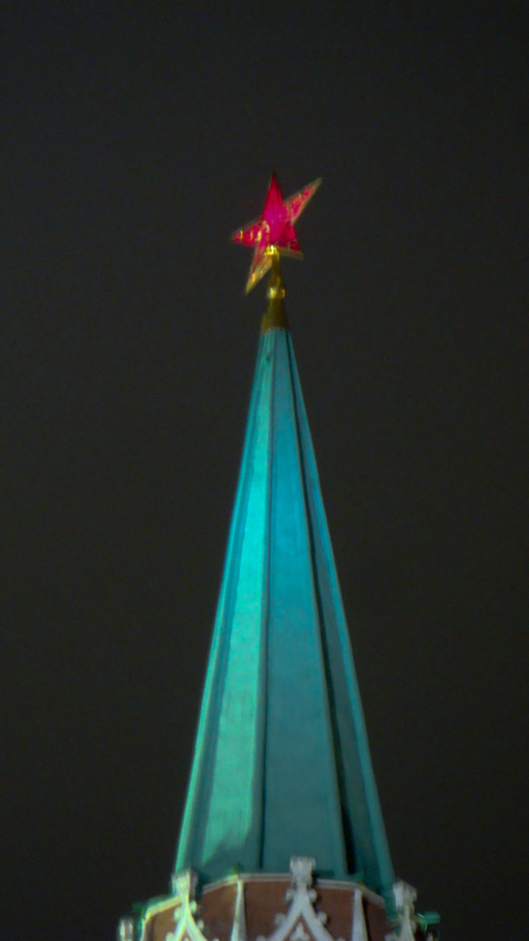 Close nighttime view of a red star crowning the steep green spire of a Moscow Kremlin tower.