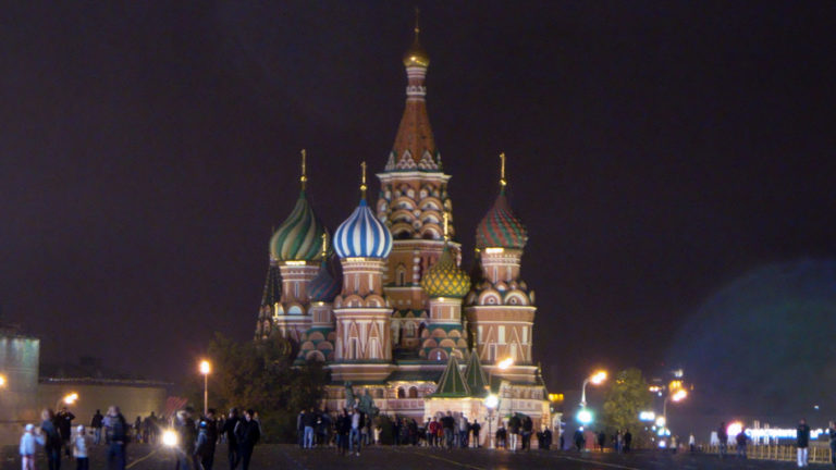 Frontal nighttime view of Saint Basil’s Cathedral with a crowd gathered along the base of the illuminated building.