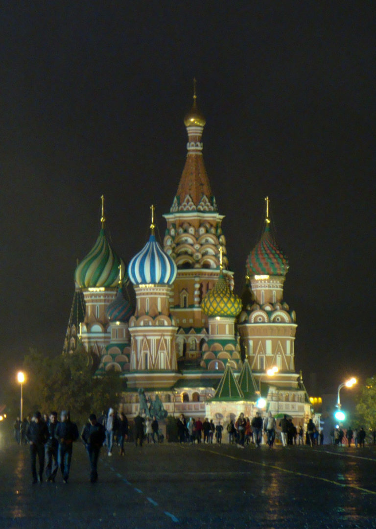 Saint Basil’s Cathedral illuminated against the night sky with visitors scattered across the plaza in front.