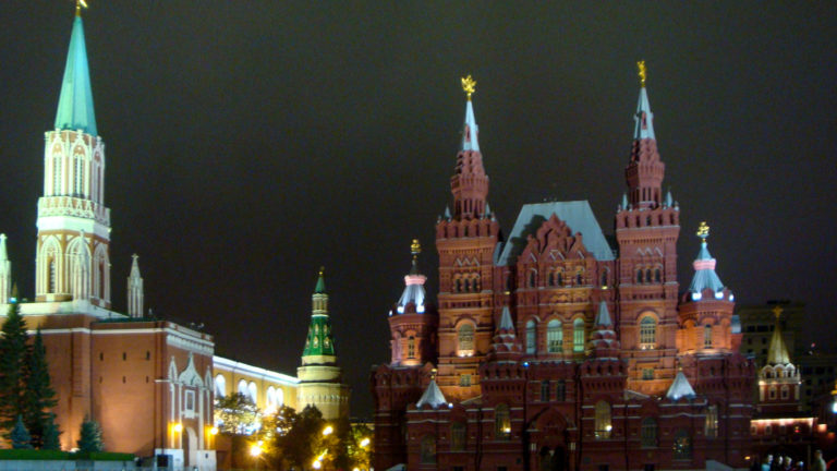 Illuminated State Historical Museum at night with its paired towers centered beside the Kremlin walls and towers.