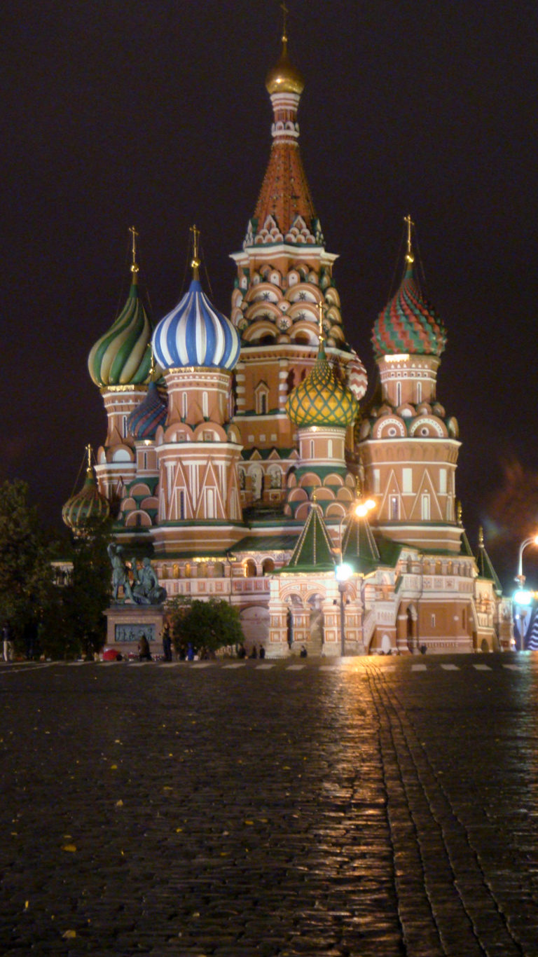 Saint Basil’s Cathedral illuminated in the distance across a broad foreground of wet, reflective Red Square cobblestones.