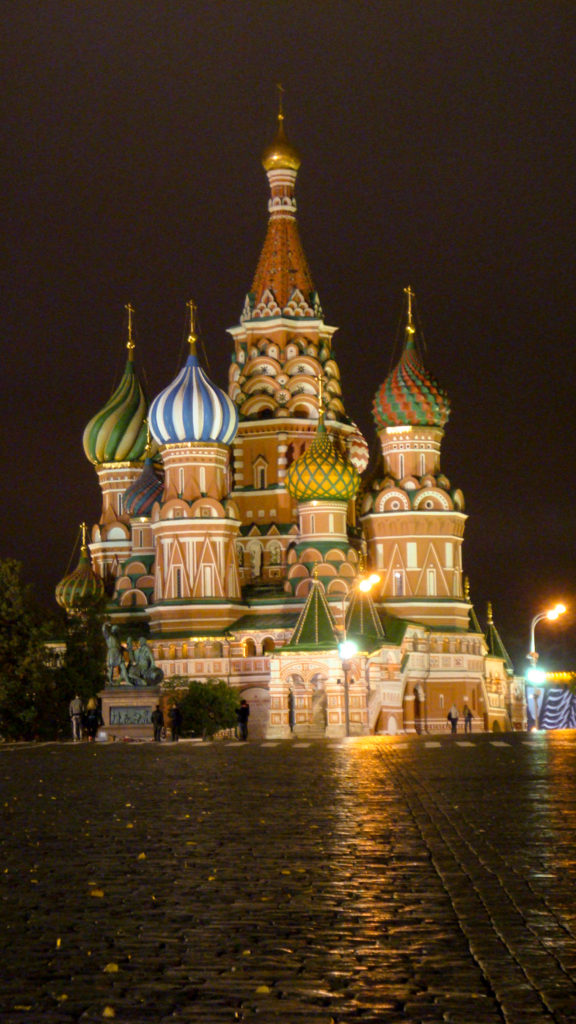 Illuminated Saint Basil’s Cathedral at night beyond wet reflective cobblestones on Red Square.