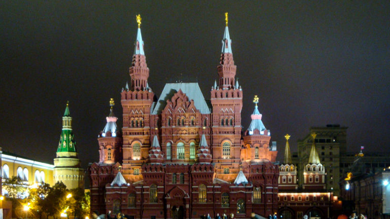 State Historical Museum brightly illuminated at night, with twin towers and nearby Kremlin buildings glowing against a black sky.