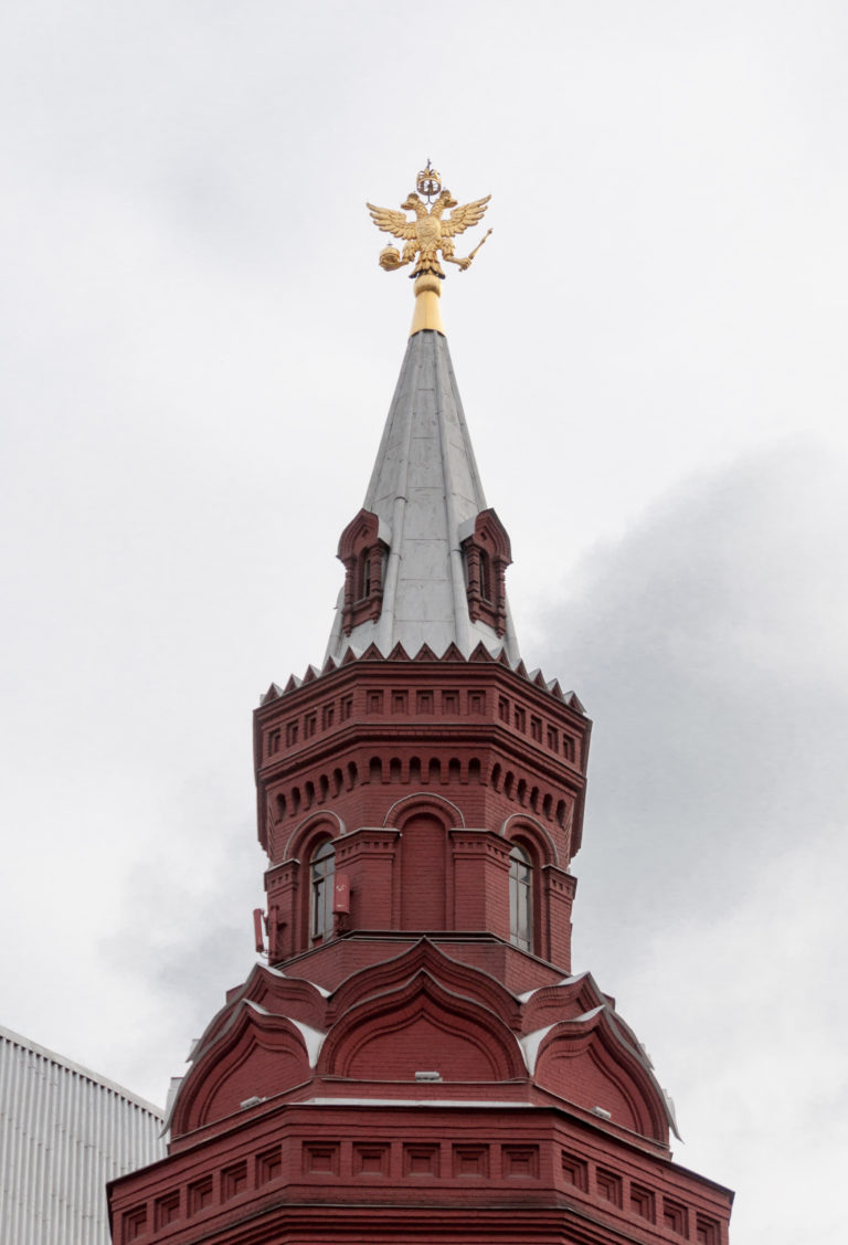 Upper red-brick tower of the State Historical Museum beneath a gray roof crowned by a gilded double-headed eagle.
