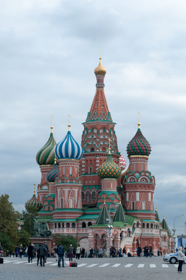 Saint Basil’s Cathedral seen across the open cobbled Red Square under a gray sky, with scattered visitors in front.