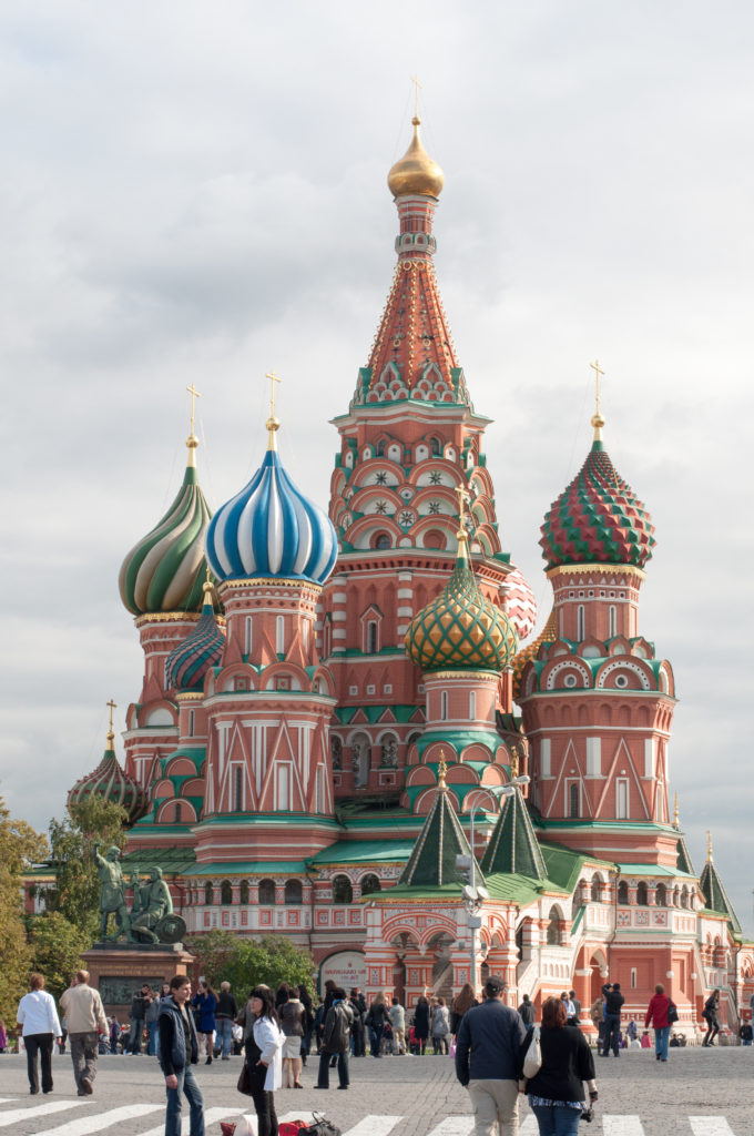 Wide frontal view of Saint Basil’s Cathedral with colorful onion domes and visitors crossing Red Square in front.