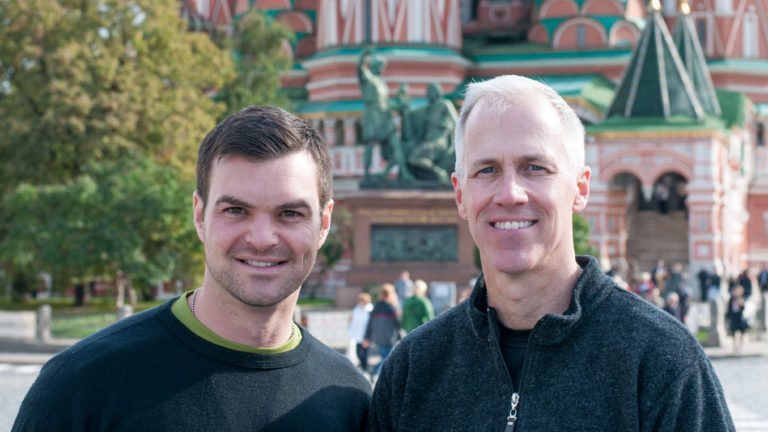 Two men standing together in Red Square with Saint Basil’s Cathedral and pedestrians behind them.