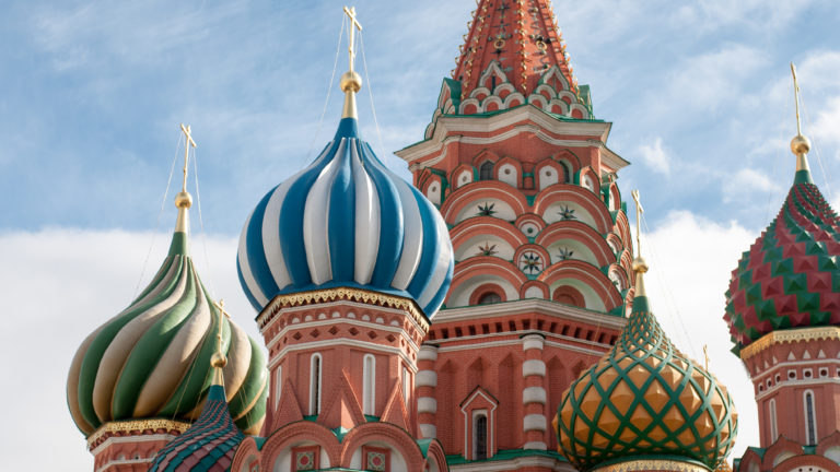 Colorful onion domes and a red central tower of Saint Basil’s Cathedral fill the frame beneath a partly cloudy sky.