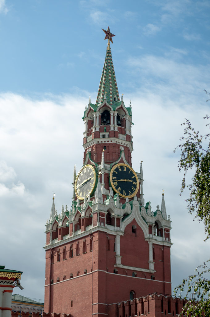 Upper Spasskaya Tower with two black-and-gold clock faces, green spire, red brickwork, and a red star.