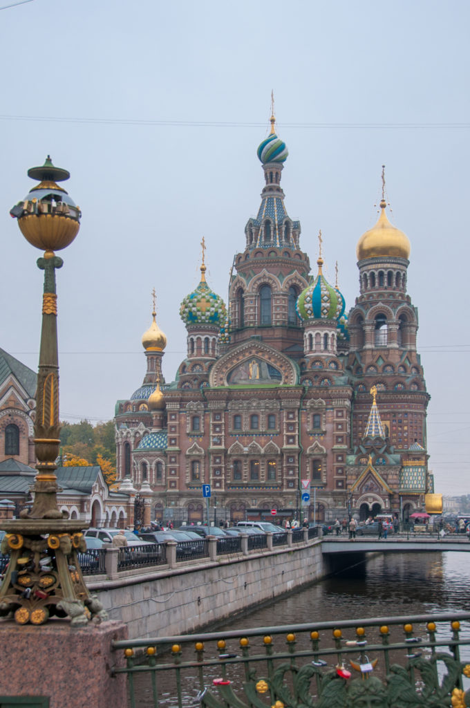 Church of the Savior on Spilt Blood across the canal, with colorful domes, gilded cupolas, an ornate street lamp, and vehicles.