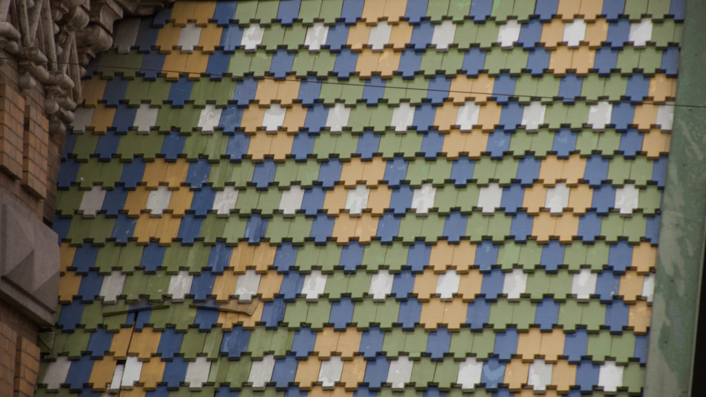 Close view of overlapping blue, green, cream, ocher, and gray glazed roof tiles arranged in repeating rows.