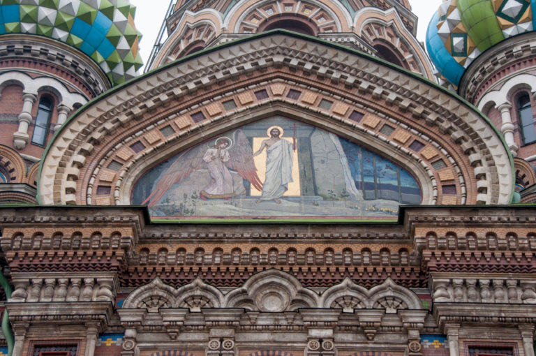 Arched exterior mosaic of Christ with attendant figures, framed by concentric molded brick arches and decorative masonry.