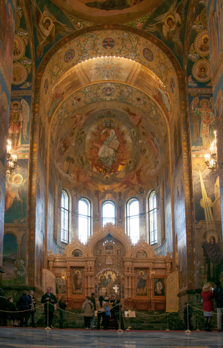 Wide interior view toward the iconostasis and tall windowed apse, with visitors standing behind barriers in the foreground.