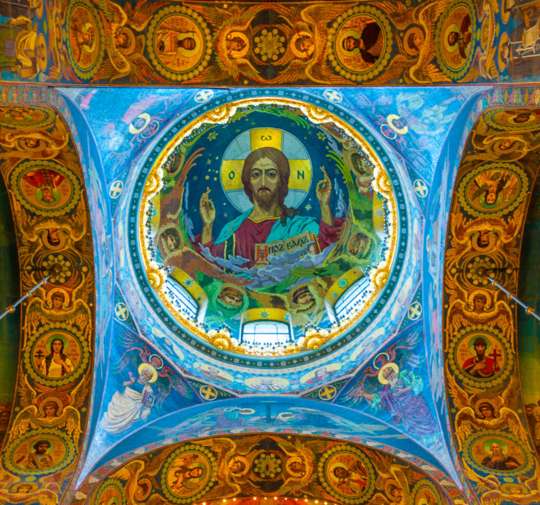 Centered upward view of the Christ Pantocrator mosaic, ringed by windows and surrounded by blue-and-gold vault decoration.