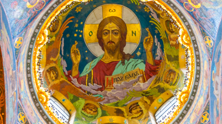 Christ Pantocrator in a circular mosaic vault, blessing with one hand and holding an open book, above small windows.