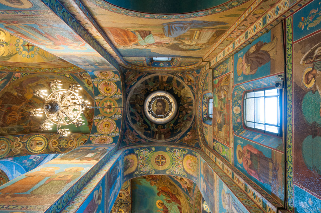Upward oblique view of mosaic-covered vaults, arches, windows, and a chandelier inside the Church of the Savior on Spilt Blood.