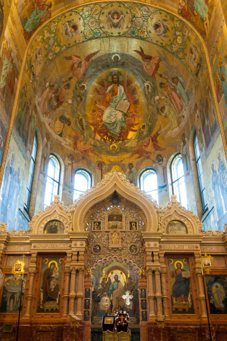 Wide sanctuary view with carved iconostasis, tall apse windows, and mosaic-covered curved ceiling above.