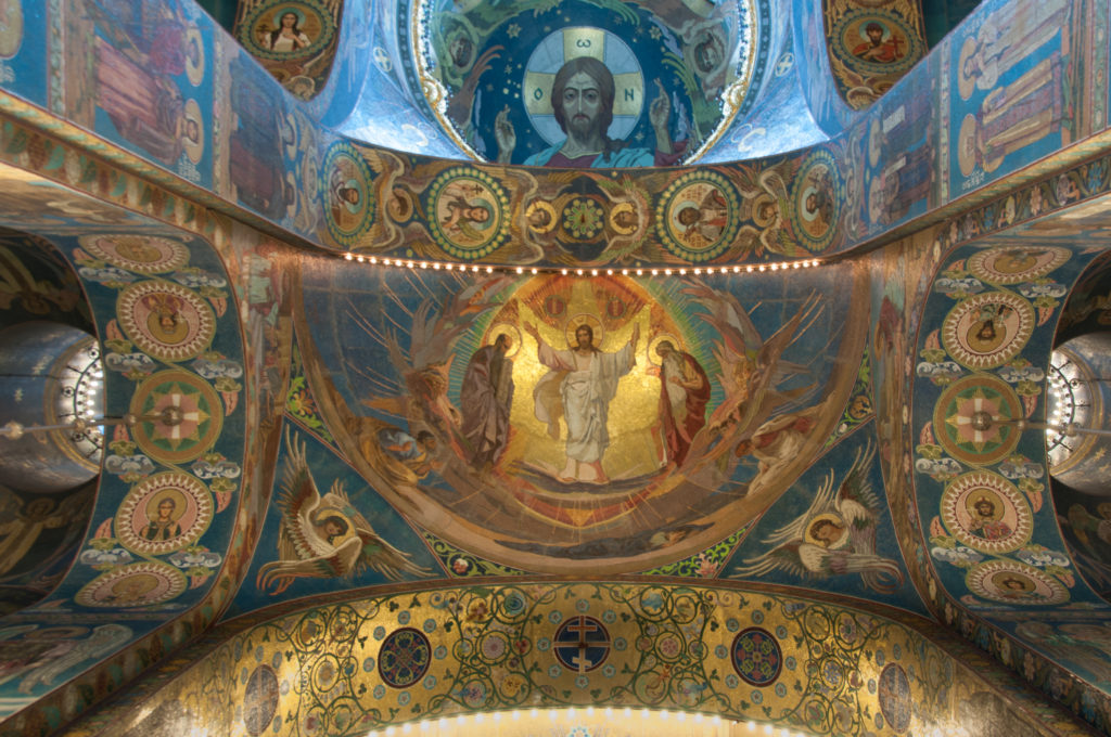 Upward interior view centered on a luminous Christ mosaic, with apostles, angels, medallions, and another Christ image above.