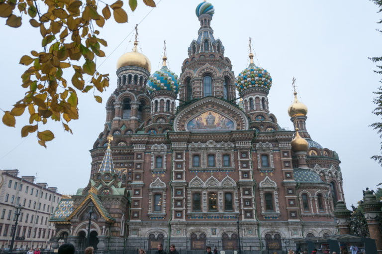 Frontal exterior of the Church of the Savior on Spilt Blood with red-brick façade, mosaic panels, and clustered onion domes.