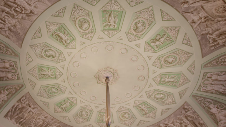 Circular pale green-and-white ceiling centered on a rosette and ringed by small figural relief panels.