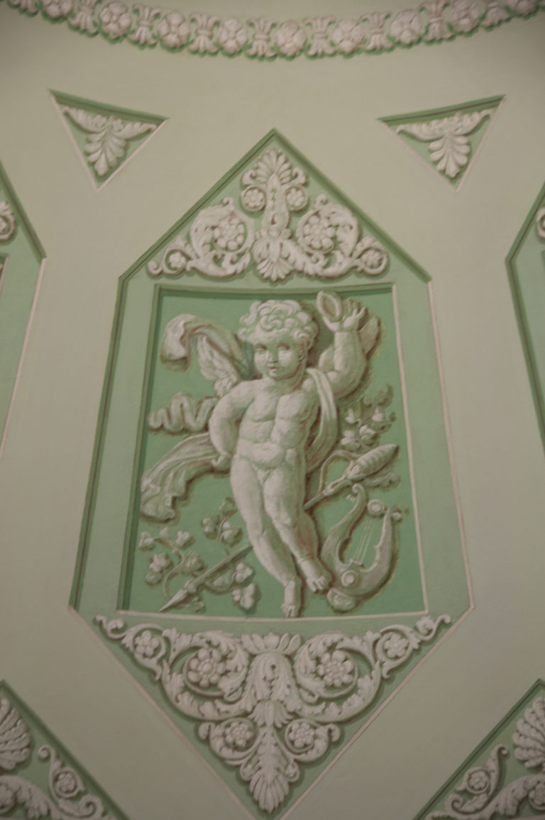 Green ceiling panel with white relief figure, scrolling foliage, and symmetrical neoclassical ornament.