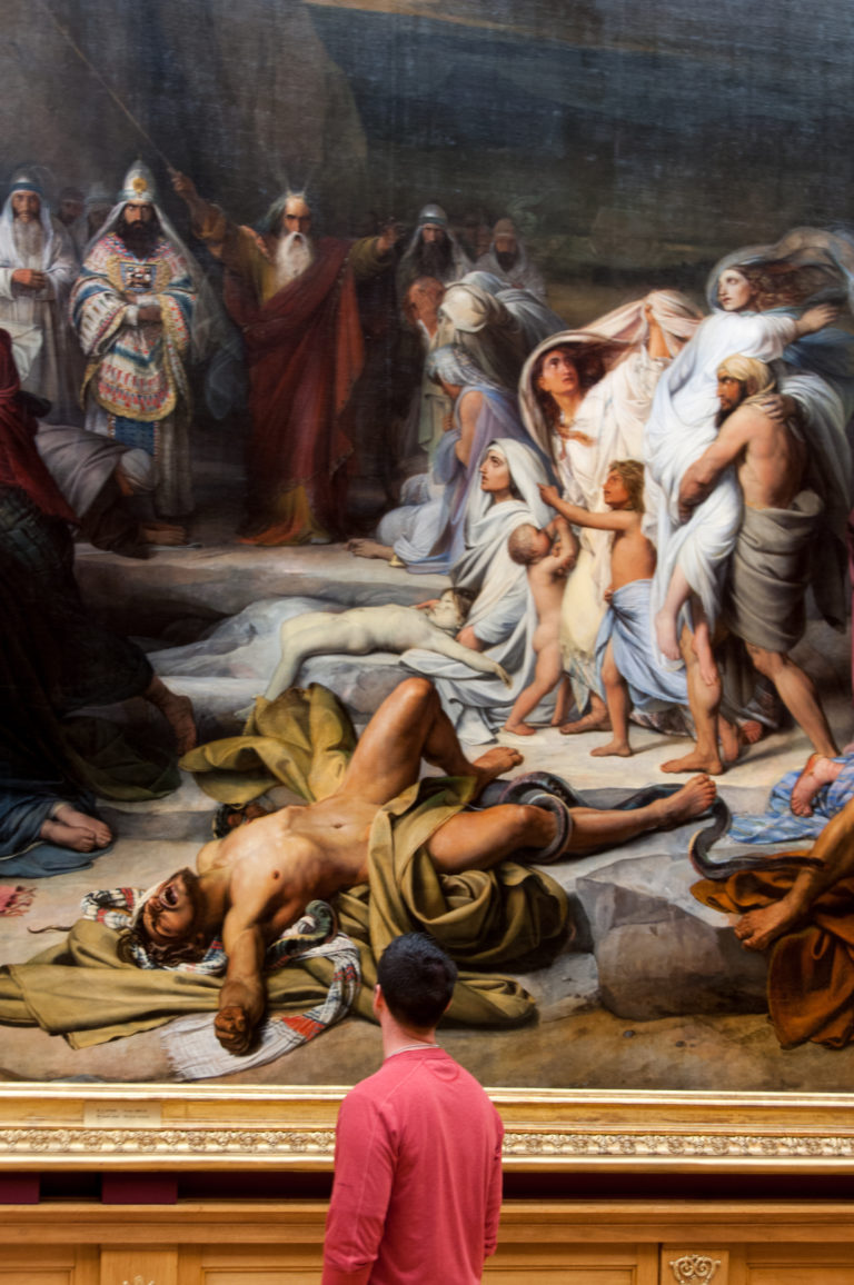 Large history painting with many figures around a fallen man, viewed above a visitor in a red shirt.