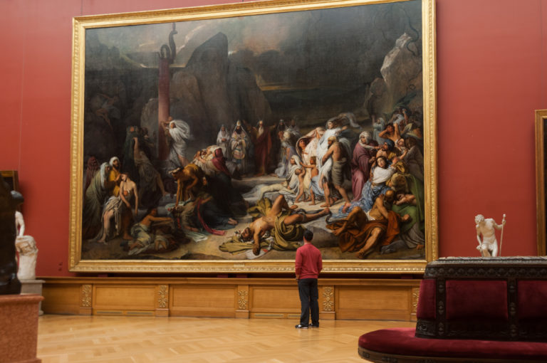 Visitor standing before Fidelio Bruni’s monumental 1841 The Brazen Serpent in a red-walled gallery with sculpture and parquet floor.