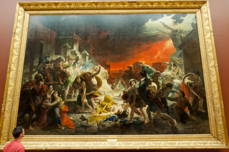 Gallery view of Karl Bryullov’s 1833 The Last Day of Pompeii, with a visitor standing beneath the monumental eruption scene.