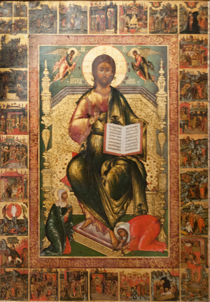 Ornate icon of enthroned Christ holding an open book, surrounded by many small narrative religious scenes.