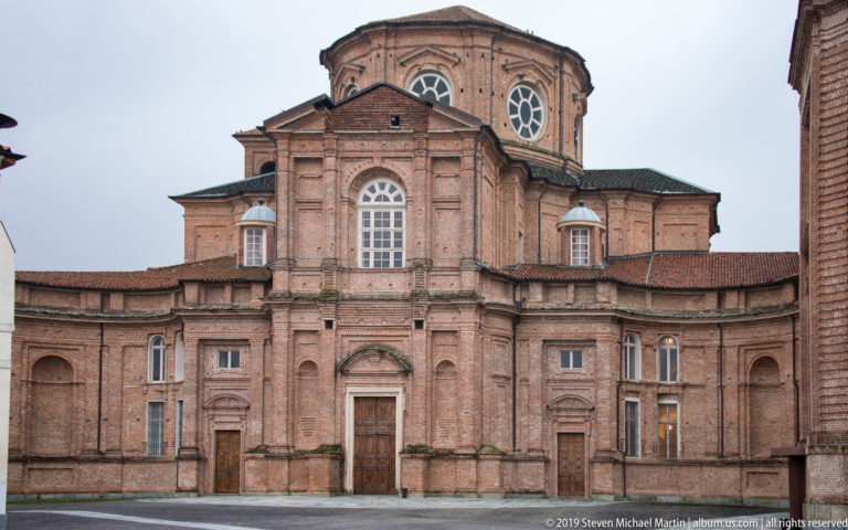 Brick façade of the Chapel of Sant’Uberto with tall arched windows, layered cornices, and a high central volume.