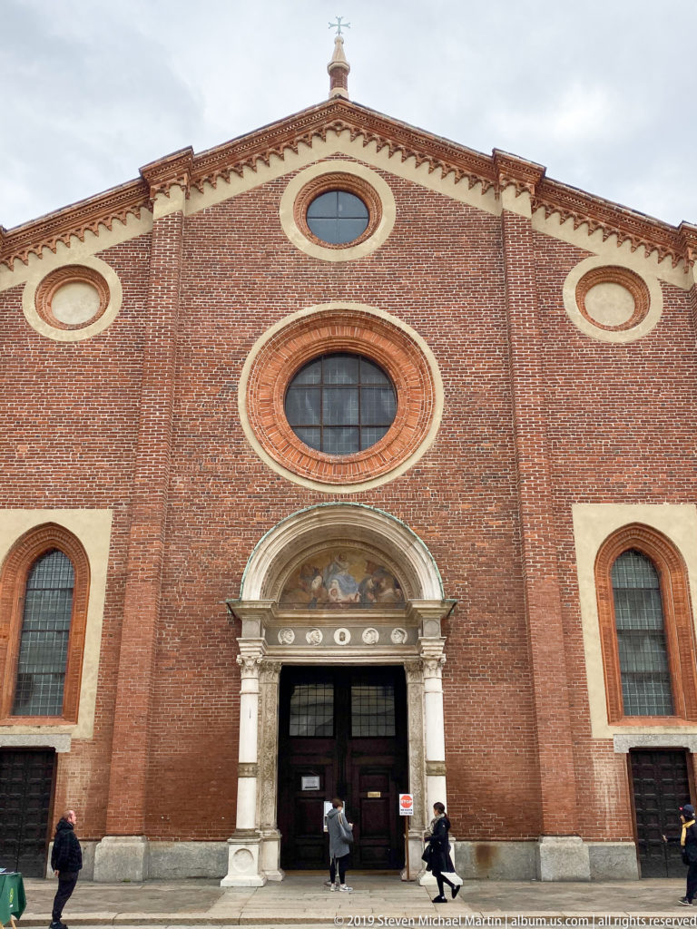 Closer frontal view of Santa Maria delle Grazie centered on the stone portal, large circular window, smaller oculi, and pointed side windows.