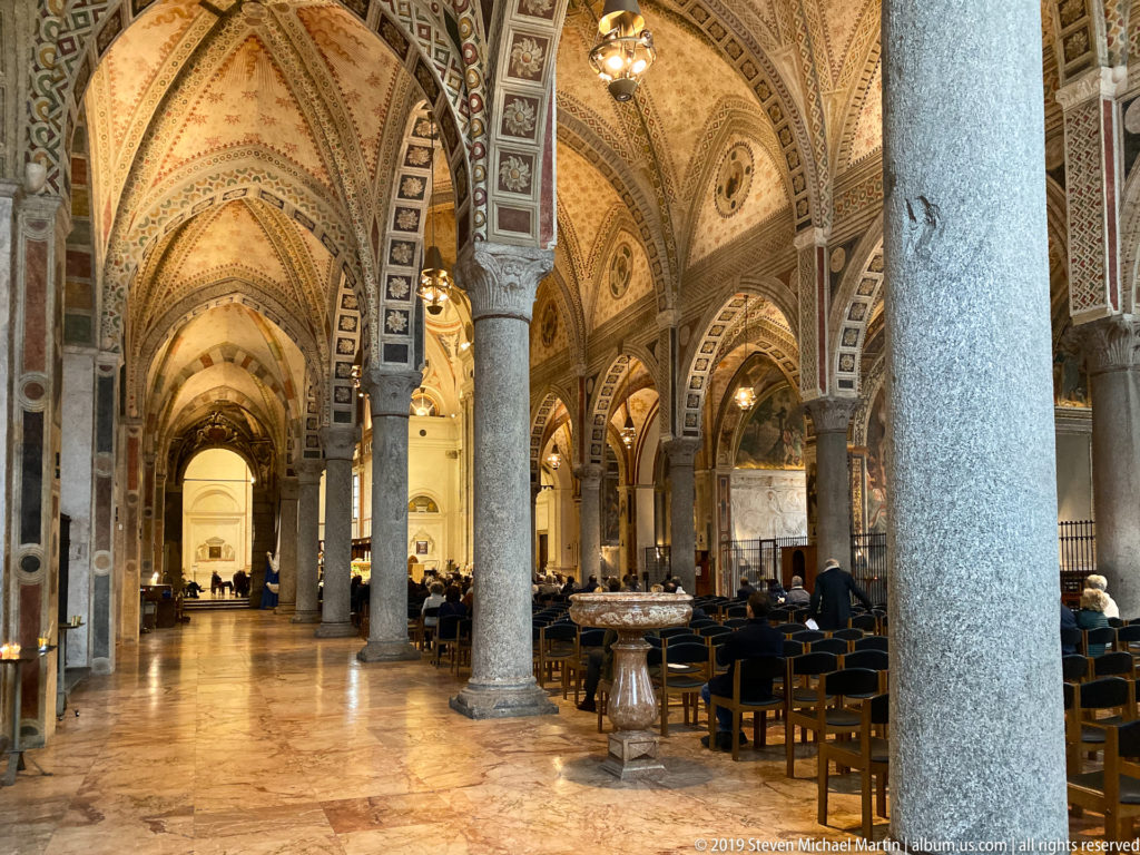 Alternate view down the richly decorated interior of Santa Maria delle Grazie with stone columns, vaulted bays, chairs, and warm lighting.