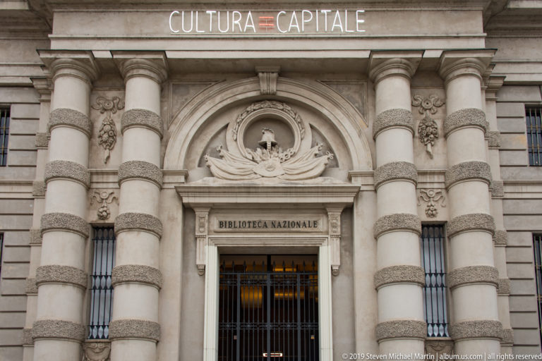 Ornate stone entrance to the Biblioteca Nazionale in Turin, with columns, carved decoration, inscription, and iron gate.