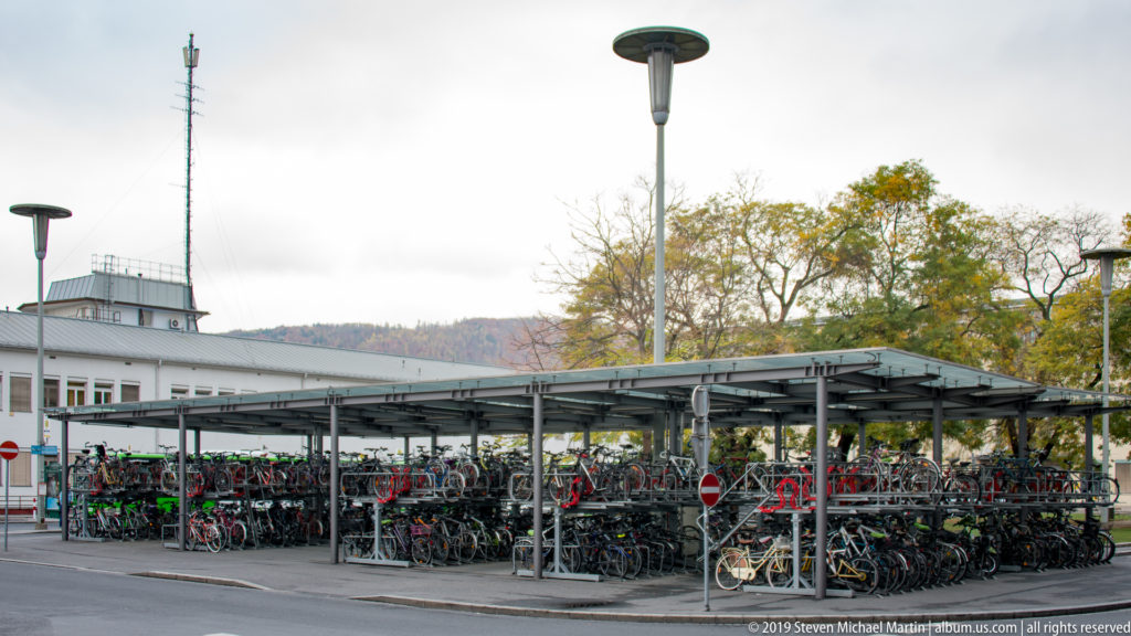 Rows of bicycles parked beneath a broad metal canopy beside a station-area street in Graz.