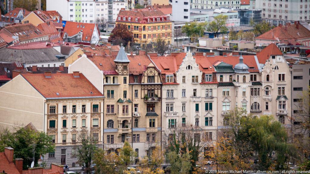 Elevated view of ornate multi-story Graz apartment façades with bay windows, balconies, gables, turrets, and red roofs.