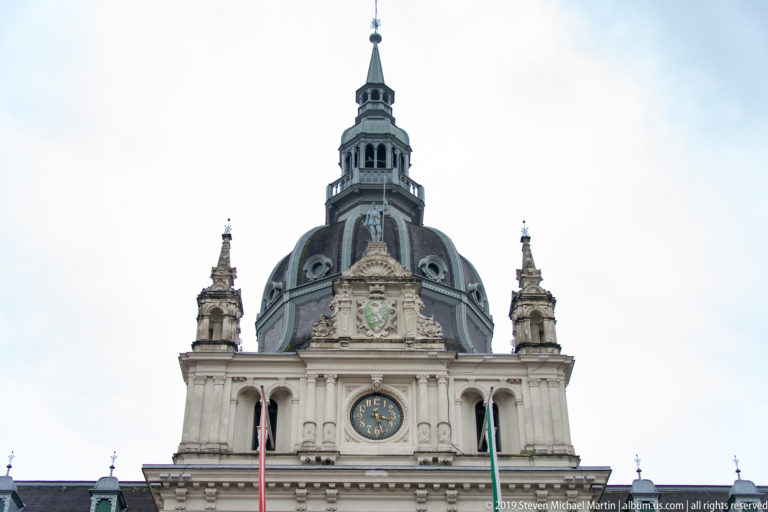 Central clock and dark domed tower of Graz Rathaus above an ornate pediment, flanked by smaller pinnacles.