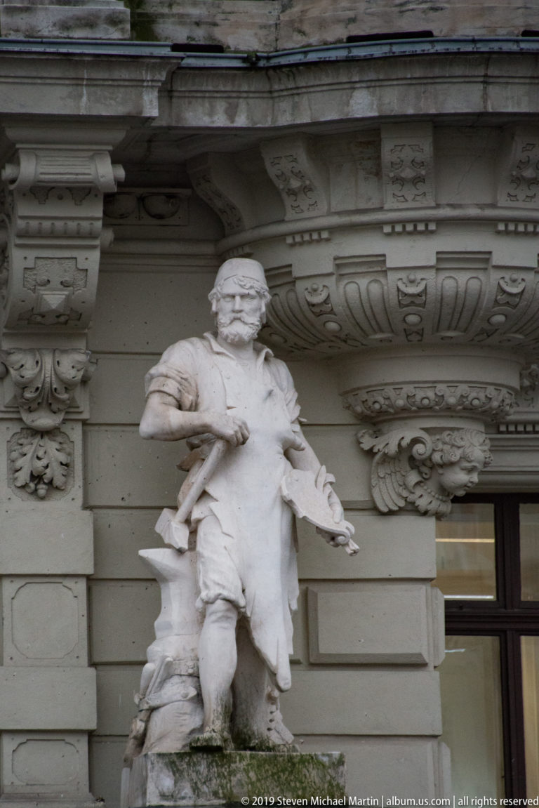 Carved male figure on the Graz Rathaus façade beneath an elaborate cornice with scrolls, brackets, and molded ornament.