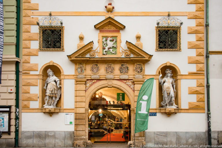 Decorated arched entrance with Styrian panther relief, coats of arms and two armored niche statues in Graz.