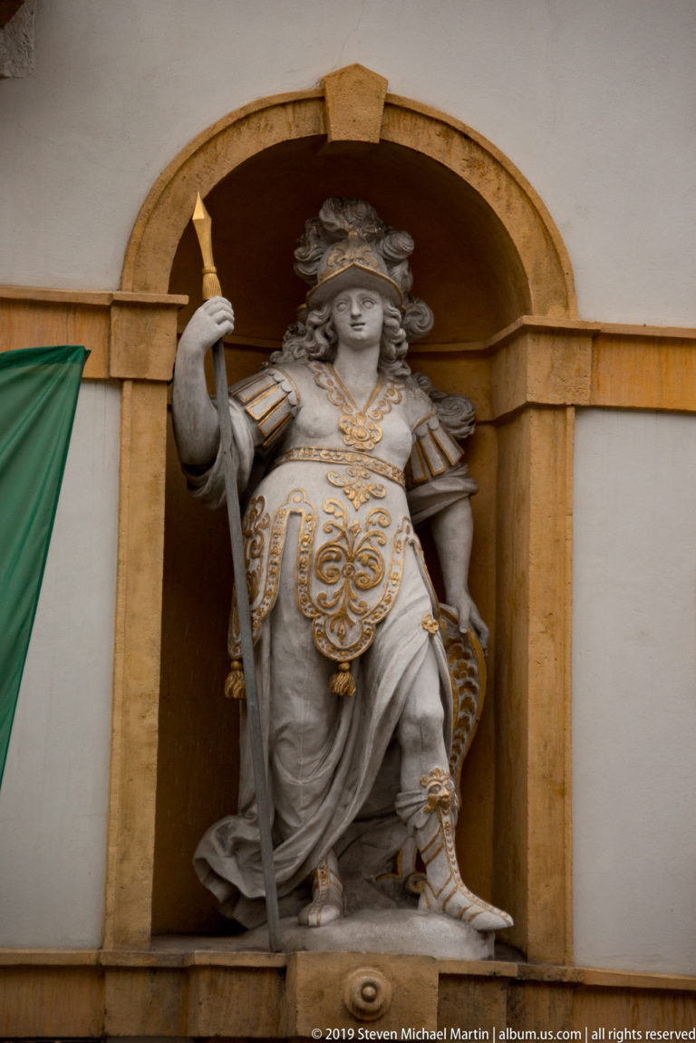 Armored stone figure with gilded costume details standing in an arched niche on a Graz façade.