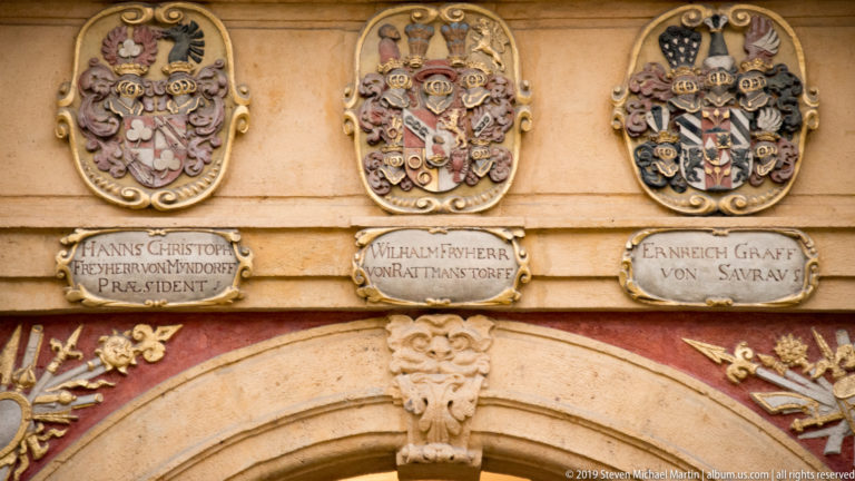 Three carved coats of arms with inscribed name plaques above a decorated arched doorway in Graz.