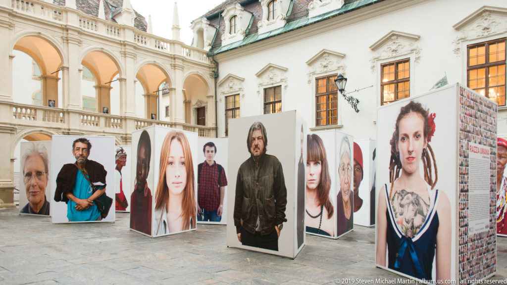Wide view of portrait panels and visitors spread through the arcaded courtyard of the Graz Landhaus.