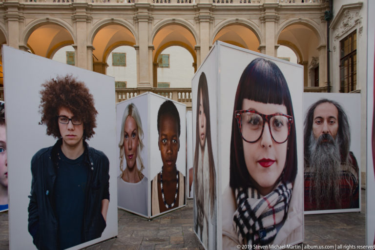 Freestanding oversized portrait photographs arranged in rows beneath arcaded galleries in a Graz courtyard.